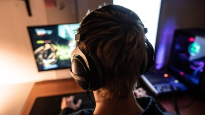 Rear View of Gamer with Headset on Playing Online Video Games in Dark Room